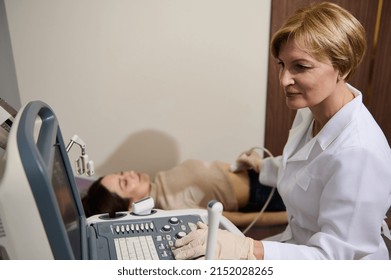 Confident Caucasian adult female doctor moves acontact probe over the abdomen of a young woman patient lying on daybed during a medical examination on an ultrasound machine. USG Pregnancy ultrasound 