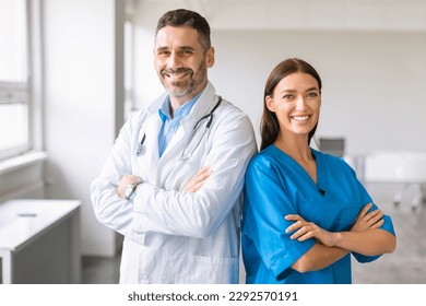 Confident caucasian colleagues male doctor and female nurse, wearing coats, posing with folded arms and smiling at camera at modern light medical office - Powered by Shutterstock