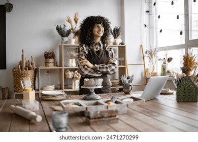 Confident Caucasian female artisan in cozy workspace surrounded by crafting materials, laptop, and decorations, embodying creativity and entrepreneurship. - Powered by Shutterstock