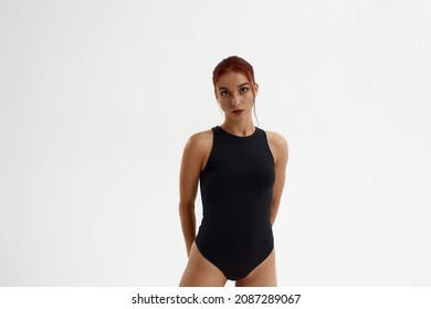 Confident caucasian female ballet dancer standing and looking at camera. Young attractive woman with red hair and wearing leotard. Girl isolated on white background. Studio shoot. Copy space