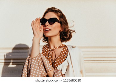 Confident caucasian girl in dark sunglasses looking in distance. Outdoor photo of good-humoured fashionable woman.