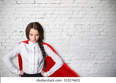Confident caucasian superwoman with red cape on white brick wall background. Power concept
