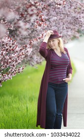 Confident Caucasian Woman With Long Blonde Hair Near Blossoming Orchard With Purple Fedora Hat