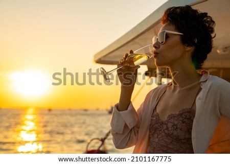 Confident Caucasian woman relax and enjoy luxury outdoor lifestyle drinking champagne while travel on catamaran boat yacht sailing in the ocean at sunset on summer beach holiday vacation trip
