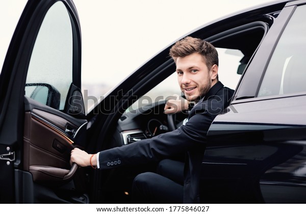 Confident Chauffeur.\
Guy in suit sitting in driver\'s seat, getting in his car at\
downtown area, closing the\
door