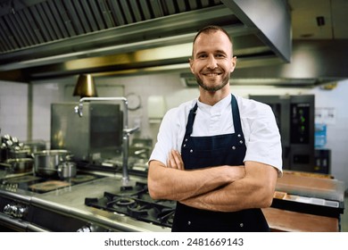 Confident chef standing with crossed arms in the kitchen at restaurant and looking at camera. 