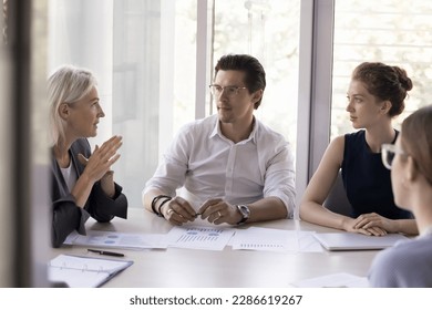 Confident company executive, boss woman talking to employees over business marketing reports on meeting. Business mentor teaching team of interns, new workers, discussing paper charts - Powered by Shutterstock