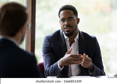 Confident Concentrated African American Male Employee Talk With Colleague Explain Thought Or Idea, Focused Biracial Businessman Speak With Coworker Or Partner, Brainstorm At Office Boardroom Meeting