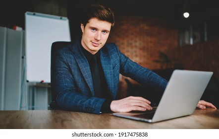 Confident Corporate Employer Using Laptop Computer During Working Time In Office Interior, Portrait Of Caucasian Businessman Looking At Camera Sitting At Desktop With Modern Netbook Technology