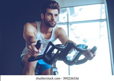 Confident cycler. Low angle view of young man in sportswear cycling at gym