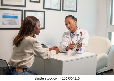 Confident Doctor Consulting Female Patient With Digital Tablet. Young African American Woman Sitting At Doctors Office And Looking At Her Diagnosis On Touchpad. Medical Consultation Concept