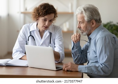 Confident doctor consulting mature patient at appointment, explaining, showing medical checkup results on laptop screen, serious young woman physician giving recommendations at meeting - Powered by Shutterstock