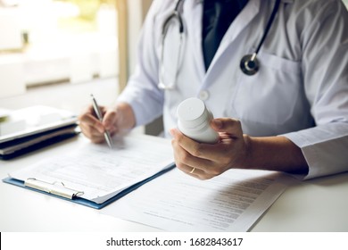 Confident doctor man holding a pill bottle and writing while talking with senior patient and reviewing his medication at office room. - Shutterstock ID 1682843617