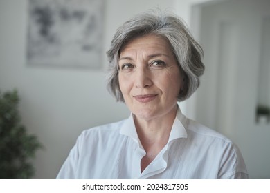 A Confident, Educated Older Lady Executive Manager Stands In A Bright Contemporary Workplace And Appearing Serious. A Senior Female Professor Or Instructor Headshot In University