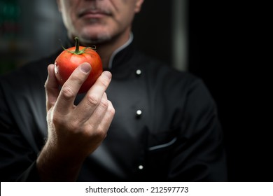 Confident elegant chef holding a delicious tomato on dark background. - Powered by Shutterstock