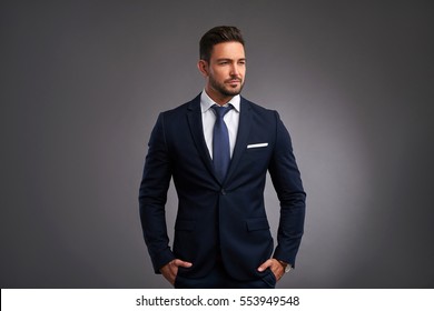 A Confident Elegant Handsome Young Man Standing In Front Of A Grey Background In A Studio Wearing A Nice Suit
