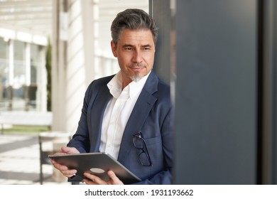 Confident Elegant Older Businessman In Suit Standing And Working With Business Tablet Computer In Office Atrium.