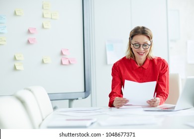 Confident Employer Reading Resumes Of Applicants While Sitting By Desk In Boardroom Before Interview