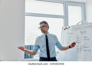 Confident English teacher pointing whiteboard while standing at the classroom - Powered by Shutterstock