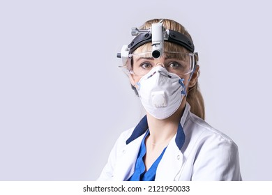 Confident ENT Doctor Wearing Surgical Headlight Head Light And Protective Glasses. Portrait Of Female Otolaryngologist Or Head And Neck Surgeon On Light Grey Background.