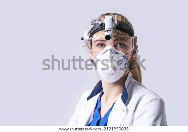 Confident ENT doctor\
wearing surgical headlight head light and protective glasses.\
Portrait of female otolaryngologist or head and neck surgeon on\
light grey\
background.