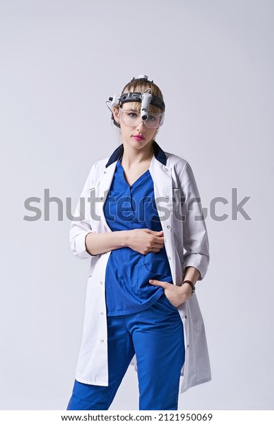 Confident ENT doctor\
wearing surgical headlight head light and protective glasses.\
Portrait of female otolaryngologist or head and neck surgeon on\
light grey\
background.