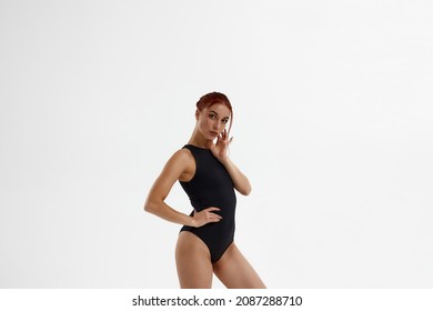 Confident european female ballet dancer standing and looking at camera. Young attractive woman with red hair and wearing leotard. Girl isolated on white background. Studio shoot. Copy space