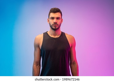 Confident european young man portrait. Handsome bearded guy wear tank top and looking at camera. Isolated on blue and pink background. Studio shoot. Copy space