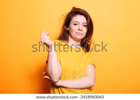 Confident female adult with brunette hair and a happy smile. She stands, looking at the camera, wearing casual clothing. Isolated orange background adds vibrancy to this cheerful portrait.