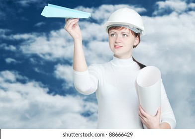 Confident Female Aeronautical Engineer With A Paper Plane And Blueprint Roll, Over A Sky Background