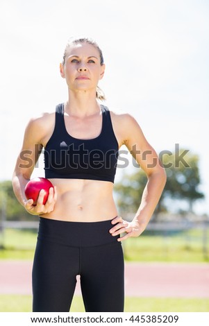 Confident female athlete holding a shot put ball in stadium