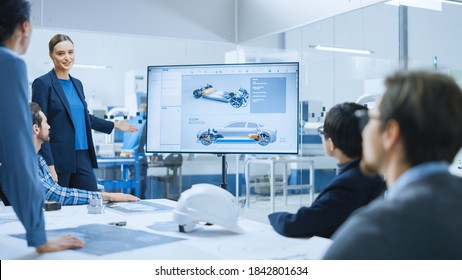 Confident Female Automotive Engineer Reports To Diverse Team Of Specialists, Managers, Businesspeople And Investors Sitting At The Conference Table, She Shows TV With 3D Prototype Of Electric Car