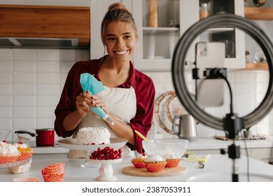 Confident female baker applying whipped cream on cake while streaming online from the kitchen - Powered by Shutterstock