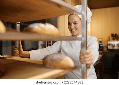 Confident female baker pulling rack of freshly baked bread - Powered by Shutterstock