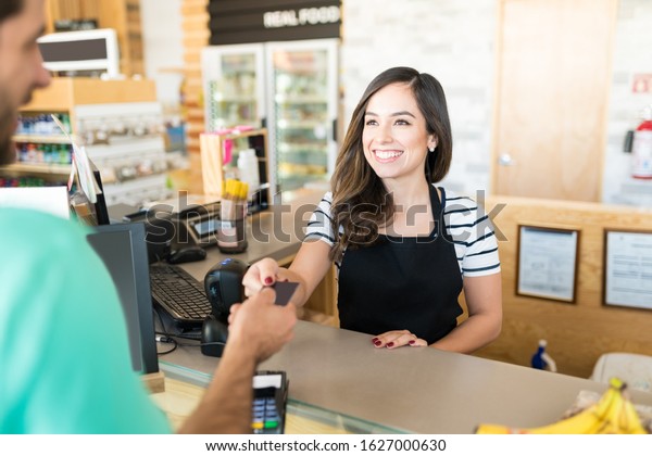 Confident female cashier receiving payment\
through credit card in\
supermarket