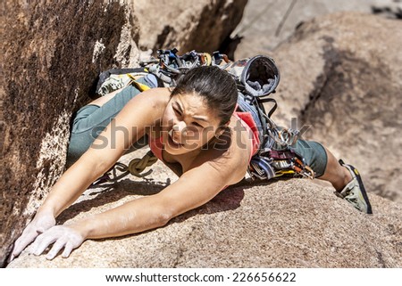 Confident female climber struggles for her next grip on the edge of a challenging cliff.