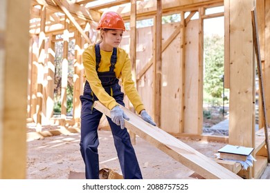 Confident Female Constructor Wearing Helmet And Uniform While Preparing Frame For Covering Roof On The Future House, Dragging Wooden Beam Into Another Place, Concentrated On Work