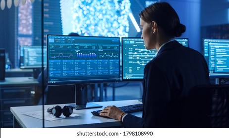 Confident Female Data Scientist Works on Personal Computer in Big Infrastructure Control and Monitoring Room with Neural Network. Woman Engineer in an Office Room with Colleagues.