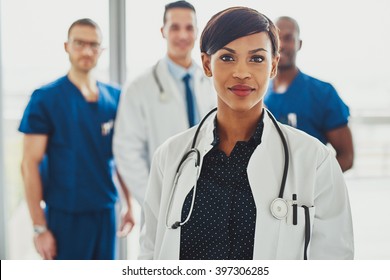 Confident female doctor in front of team, looking at camera smiling, multiracial team with black female doctor