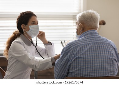 Confident female doctor wearing face mask checking mature man lungs, using stethoscope, listening to elderly patient heartbeat, breath, elderly generation healthcare, medical checkup concept