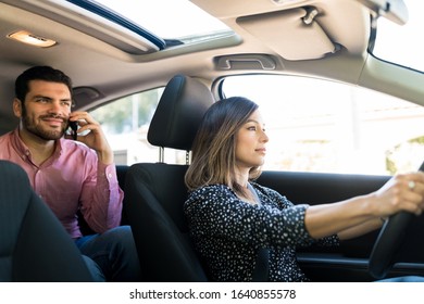 Confident female driver driving taxi while male passenger using cellphone in car - Shutterstock ID 1640855578