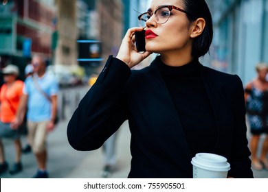 Confident Female Executive Manager With Trendy Red Lips Talking On Phone About Work Strolling With Coffee To Go, Serious Business Woman In Black Elegant Formal Wear Having Mobile Conversation Outdoors