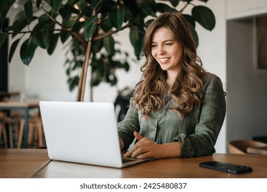 Confident female freelancer using a laptop for remote work sitting at the desk in a cozy cafe. An intelligent young woman answering emails, web surfing indoor, side view - Powered by Shutterstock