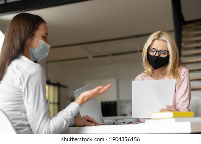 Confident Female Hr Manager Sitting At The Office, Wearing Face Mask, Training Young Female Worker Intern, Interviewing Job Seeker, Mentoring A Student. Social Distance And Safety At Work Concept