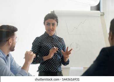 Confident Female Indian Conference Speaker Coach Training Diverse Employees Group Give Flip Chart Presentation At Office Meeting, Hindu Business Woman Presenter Teach Staff Team At Corporate Workshop