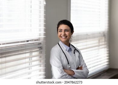 Confident Female Indian Doctor Standing By Window, Looking Away With Happy Smile. Young General Practitioner, Therapist Thinking Of Future Career Vision, Enjoying Success. Head Shot Portrait