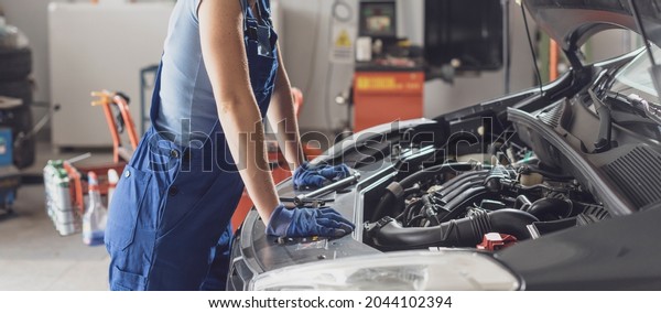 Confident female mechanic working in the auto\
repair shop, she is checking a car\
engine