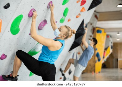 Confident female mountaineer protective mask climbing artificial rock wall without belay indoors - Powered by Shutterstock