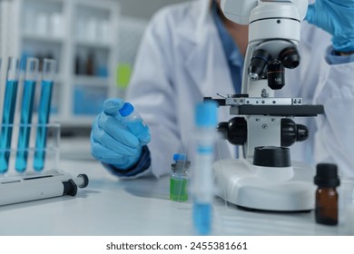 Confident female scientist conducting research in medical laboratory A researcher in the foreground is using a microscope. Medical test tube. - Powered by Shutterstock