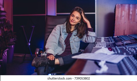 Confident Female  Sitting By Audio Mixing Console In Sound Recording Studio. Female Music Composer Sitting By Sound Mixing Console.